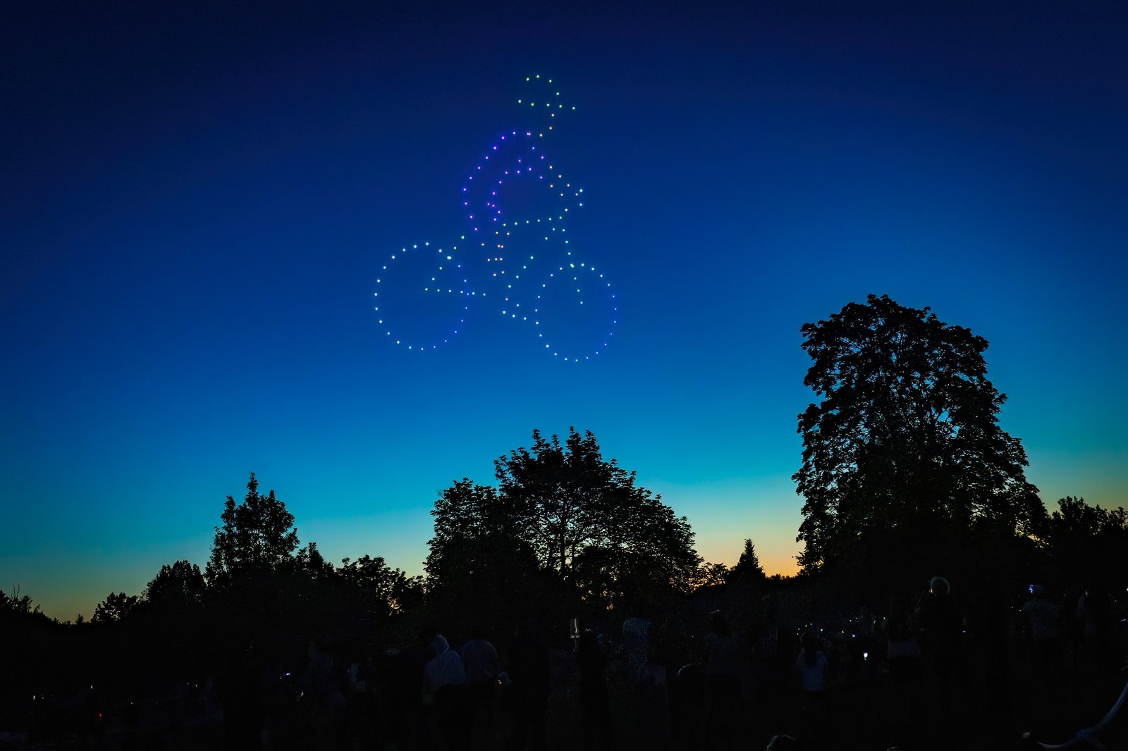 Spectacle de drones lumineux dessinant un cycliste dans le ciel au crépuscule